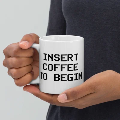 A person holding a white glossy ceramic programmer coffee mug featuring a white "Insert Coffee To Begin" design - Funny Programmer Mugs