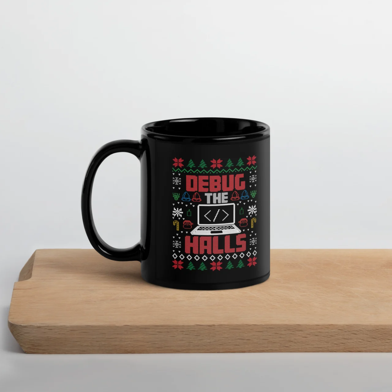 Black ceramic Debug The Halls Ugly Christmas Sweater Mug sitting on a wooden surface, featuring a colorful Ugly Christmas Sweater pattern with the text "DEBUG THE HALLS" and a laptop graphic. This is a funny Programmer Holiday Mug.