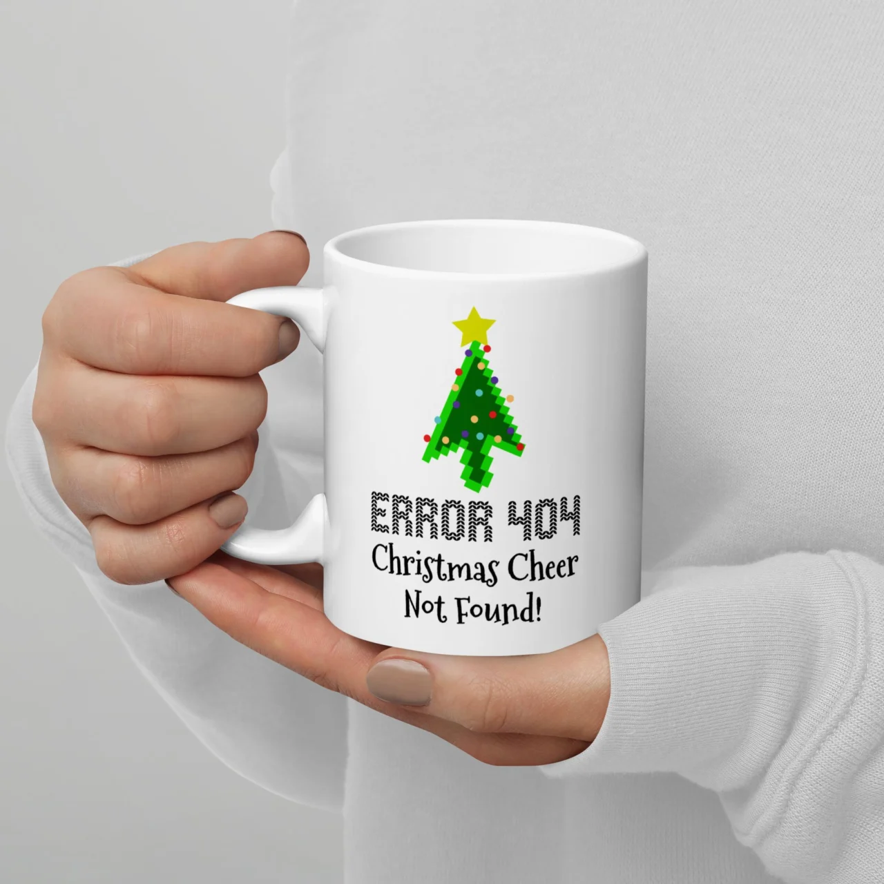 White ceramic ERROR 404 Christmas Cheer Not Found Mug held by hands, featuring a pixelated green Christmas tree and the text "ERROR 404 Christmas Cheer Not Found!" This is a funny Programmer Christmas Mug