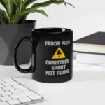 Black ceramic ERROR 404 Christmas Spirit Not Found Mug sitting on a desk next to a plant and books. The mug features a yellow warning triangle with a Christmas tree graphic and the text "ERROR 404 CHRISTMAS SPIRIT NOT FOUND." This is a funny Black Programmer Mug.