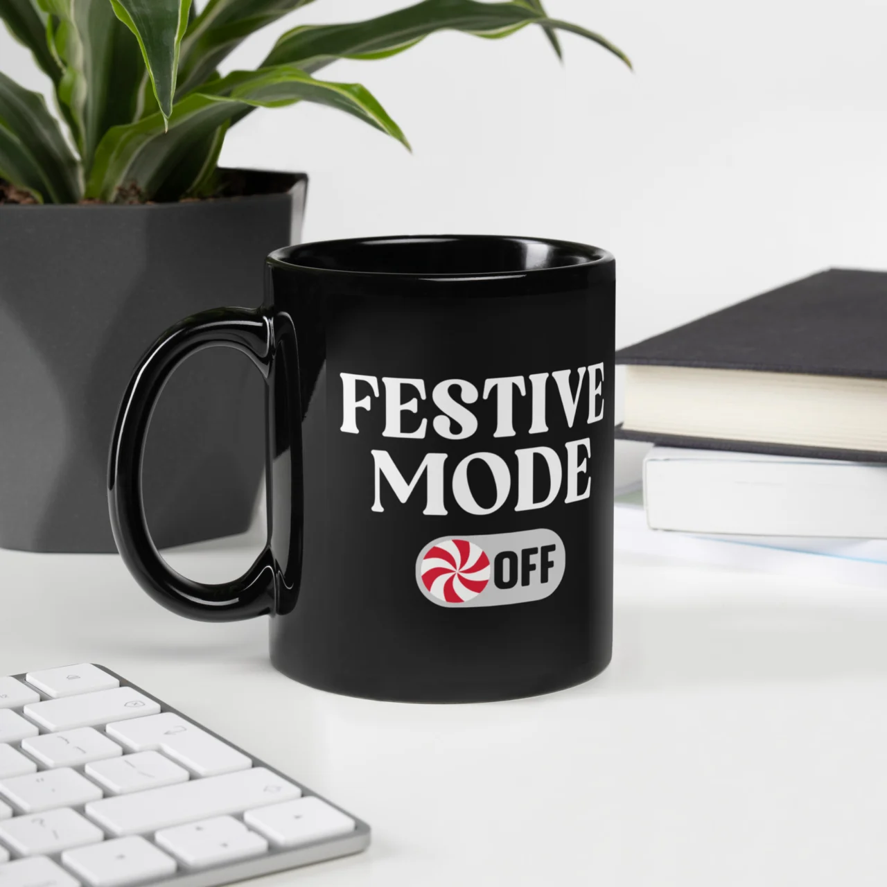 Black ceramic Funny Programmer Christmas Coffee Cup sitting on a white desk next to a keyboard. The mug features the text "FESTIVE MODE OFF" with a peppermint candy graphic on the bottom. This is a funny Programmer Christmas Mug.