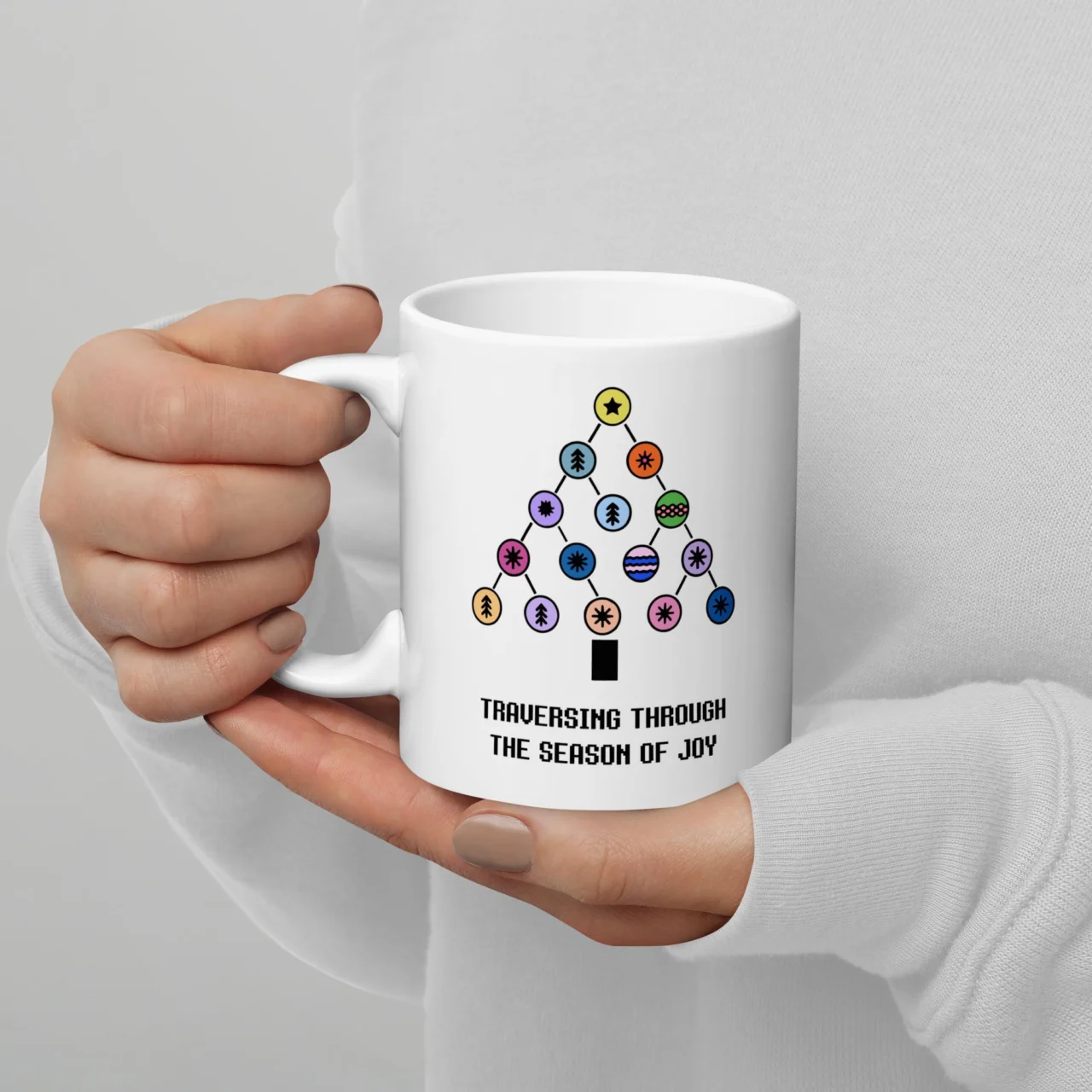 White ceramic Traversing The Season of Joy Mug held by hands, featuring a graphic of a decorated Binary Tree and the text "TRAVERSING THROUGH THE SEASON OF JOY." This is a funny Computer Science Christmas Mug.