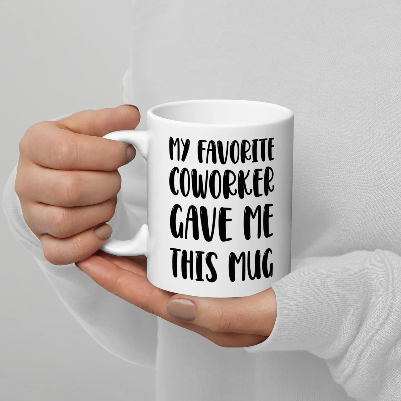 A white ceramic Sarcastic Employee Appreciation Cup held in two hands, featuring black hand-lettered text that reads "MY FAVORITE COWORKER GAVE ME THIS MUG". This is a Funny Favorite Coworker Office Mug