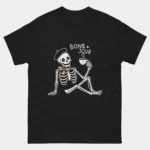 Black Bone Jour Funny French Skeleton Shirt showing a relaxed skeleton wearing a beret and holding a coffee cup with the text Bone Jour above, cute French language pun humor graphic tee