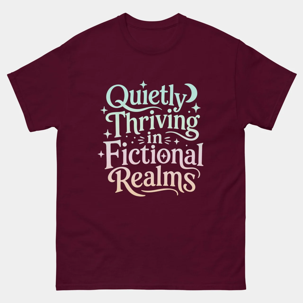Maroon cozy Quietly Thriving in Fictional Realms Book Tee with elegant multi-color typography reading Quietly Thriving in Fictional Realms decorated with moon and star accents, fantasy reader and book lover graphic tee